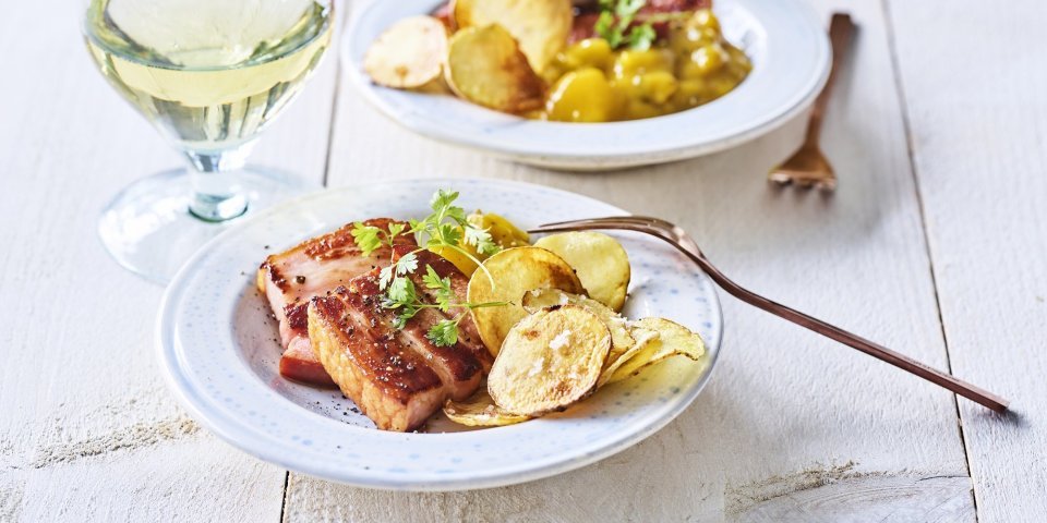 Er staan twee bordjes op tafel gevuld met krokant buikspek, krokante aardappelchips en een schep Belgische pickles. Een voorgerechtje boordevol Belgische topproducten! 