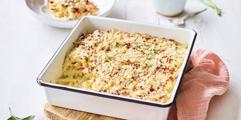 Een heerlijke gevulde ovenschotel boordevol comfortfood staat op de tafel te blinken. Onze mac and cheese met Belgische kazen zit in een witte ovenschotel met donker blauw randje, zoals bij de bomma. Er ligt een zalmroze servette langs en de een takje verse peterselie voor extra kleur in het beeld. 