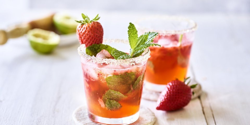 Mojito van aardbeien Twee roodgekleurde mojito's op de tafel, afgewerkt met verse munt en nog een aardbei. Alleen al kijken is een feestje, tijd om die cocktail te benuttigen. Het glad kreeg zelfs een suikerrandje.