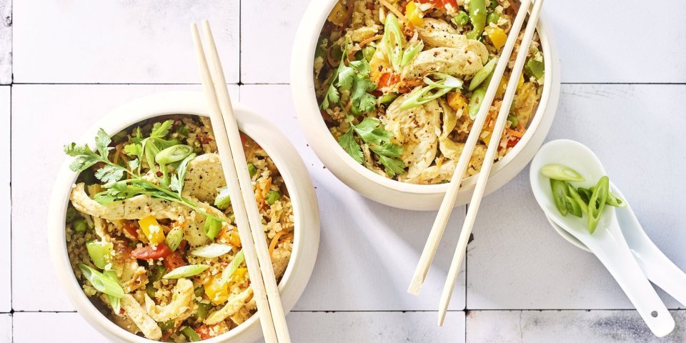 Nasi goreng van bloemkoolrijst met paprika, erwtjes en kip Twee kommetjes staan op het aanrecht. Wij maakten een op-en-top Belgische variant op de Nasi goreng, nl eentje met bloemkoolrijst, paprika, erwtjes en kip van bij ons.