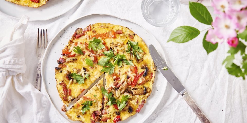 Een kleurrijke en rijkgevulde omelet met paprika, spek en champignons ligt op het bord om aan te vallen. 