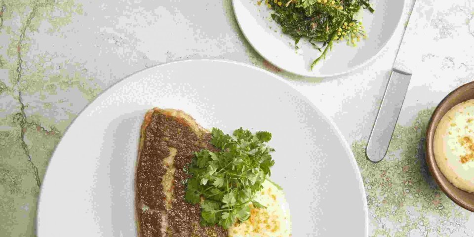 Op de graat gebakken tongschar met boerenkool Een volledige tongschar krokant gebakken ligt op een groot wit bord met boerenkool en puree erbij geserveerd.