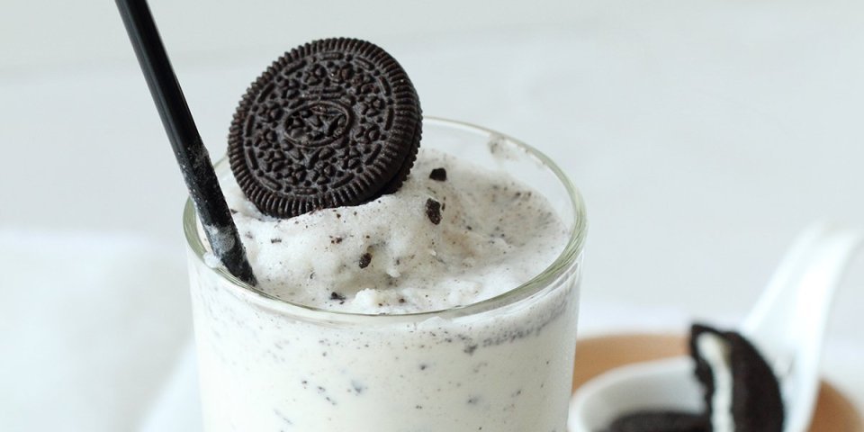 In een groot glas zit onze huisgemaakte milkshake van melk met oreokoekjes. Hij heeft dus een witte kleur met zwarte stipjes. Hij is afgewerkt met een volledig koekje aan de rand van het glas. Oreo-milkshake