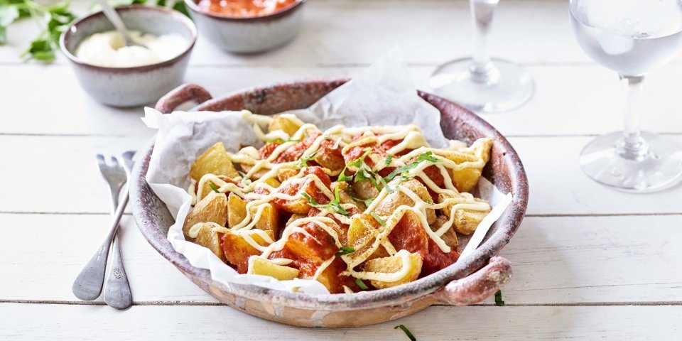 Patatas bravas Heerlijke patatas bravas geserveerd in een groot diep bord, afgewerkt met een pittige tomatendip en aïoli. Twee gekoelde watertjes staan rechts van het bord. Klaar om de tapas tafel aan te vallen.