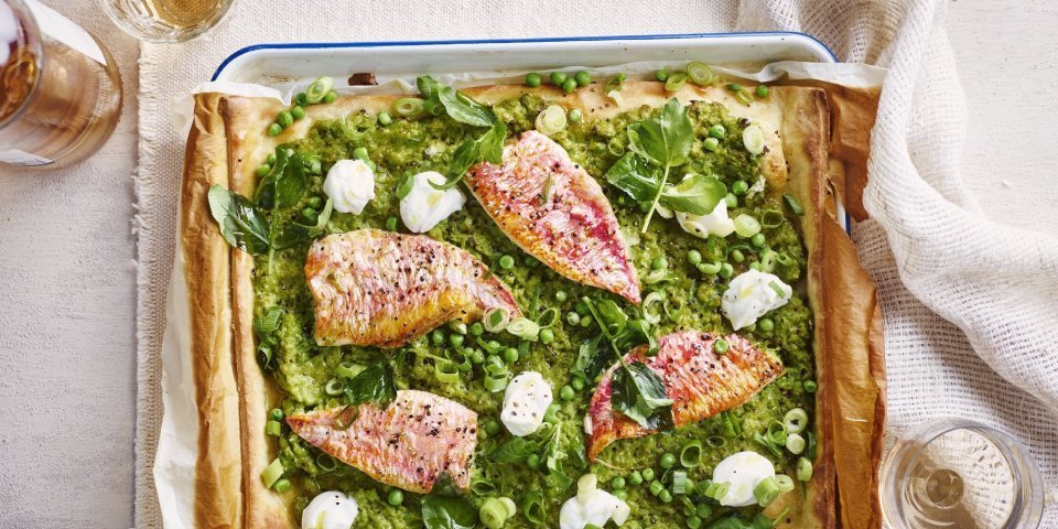 Plaatpizza met erwtenspread, waterkers en zeebarbeel Een plaatpizza staat op het midden van de tafel, klaar om aan te vallen. De plaatpizza kleurt mooi groen door de spread van erwten, hij is afgewerkt met toefjes verse kaas, blaadjes waterkers en de gebakken vis.