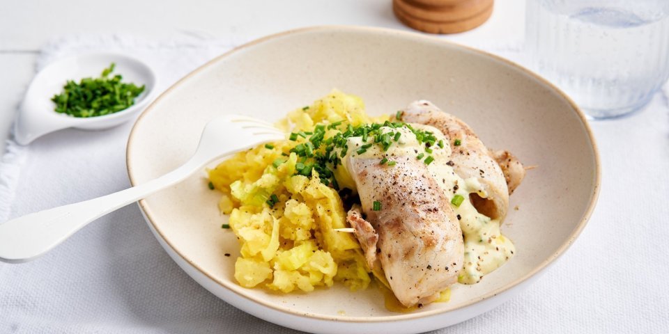 Preipuree met zeebaarsrolletjes en yoghurtsausje Op het aanrecht staat een portie eten klaar. Een schep preipuree met hierop twee visrolletjes van de zeebaars, afgewerkt met een koud sausje op basis van yoghurt.