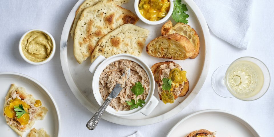 Homemade rilette zit in een porseleine potje met een smeermesje bij. Er ligt gegrilde stokbrood bij om zelf aan de slag te gaan. We dienen hem op met wat mosterd of pickles, aan jou de keuze welke je favoriet is. 