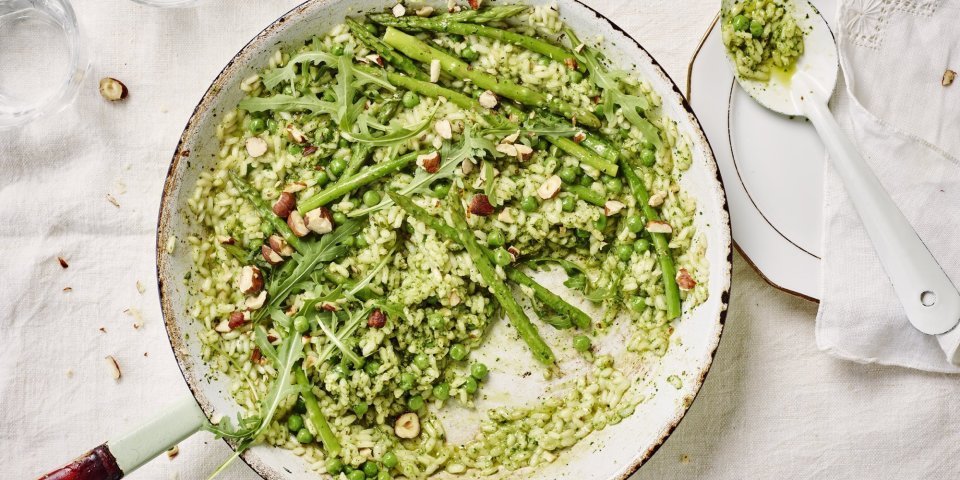 Risotto met hazelnootpesto, erwtjes en groene asperges De pan op tafel en scheppen maar. De risotto heeft een mooie groene kleur door de huisgemaakte pesto. We serveren hem met een portie extra groene groentjes zoals erwtjes, groene apserges en rucola.