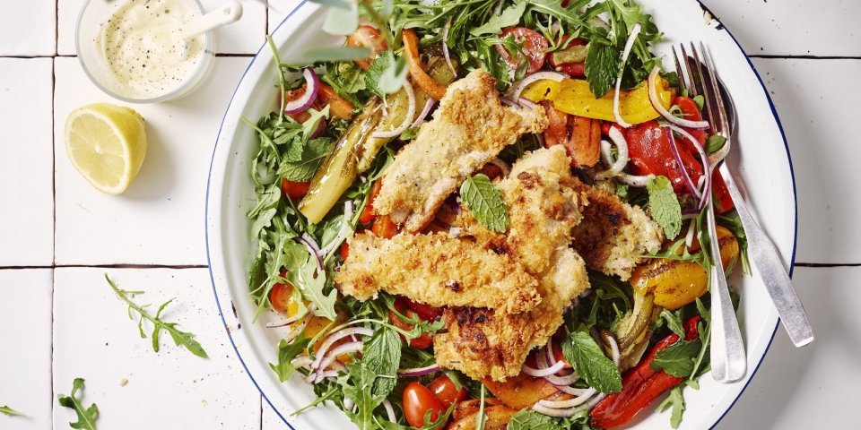 Salade met gegrilde groenten, krokant konijn en aïoli Een rijkgevulde sla met gegrilde groenten en stukjes konijn is geserveerd in een groot wit bord met blauw randje, waarvan iedereen kan opscheppen. Het staat op witte Marokkaanse tegeltjes. Er ligt een halve citroen bij en de aïoli is apart in een glaasje geserveerd.
