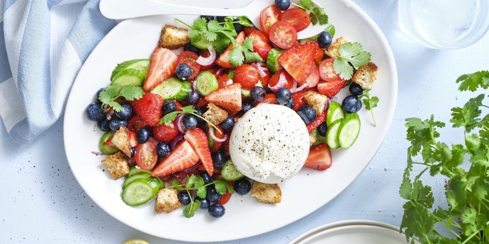 Er staat een grote schaal op tafel boordevol zomerse toppers. Denk maar aan tomaatjes, aardbeien, bosbessen, komkommers en burrata. Dit geeft echt verfrissing tijdens een zwoele zomerdag. Er ligt een citroentje langs, een glas water en verse kroiander.