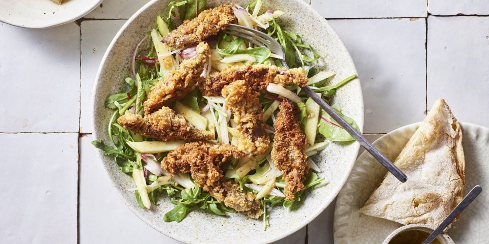 Salade met krokante leverreepjes en mosterddressing Er staat een diep bord op het aanrecht, gevuld met meerdere slasoorten en krokant gebakken leverreepjes. De mosterdressing staat er langs om zelf toe te voegen.
