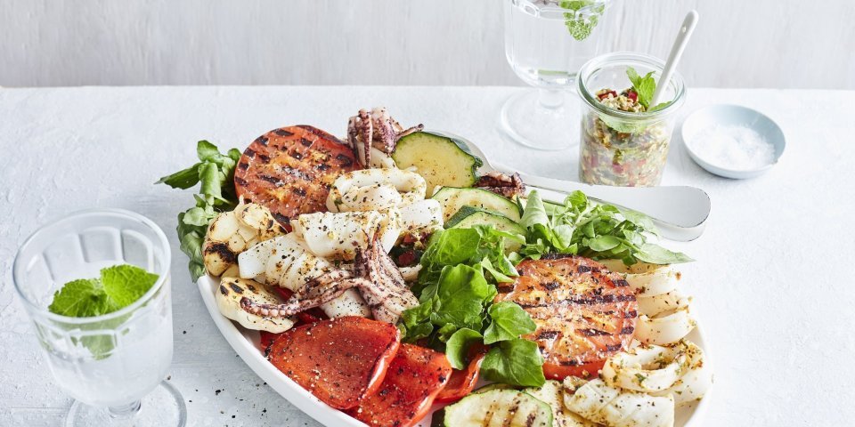 Salade van inktvis in pittige marinade en gegrilde groenten Een grote schaal gevuld met de salade van inktvis en gegrilde groenten zoals tomaten, paprika en courgette. Een topper in het zuiden boordevol zomerse ingrediënten van bij ons.