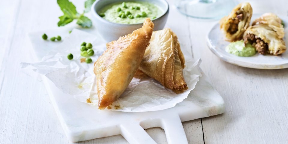 Samosa met lam en een dip van munt en erwtjes Klaargemaaakte samosa met lamsvlees liggen gepresenteerd op een marmer plankje. Ze worden opgediend met een frisgroene dip van munt en erwtjes.
