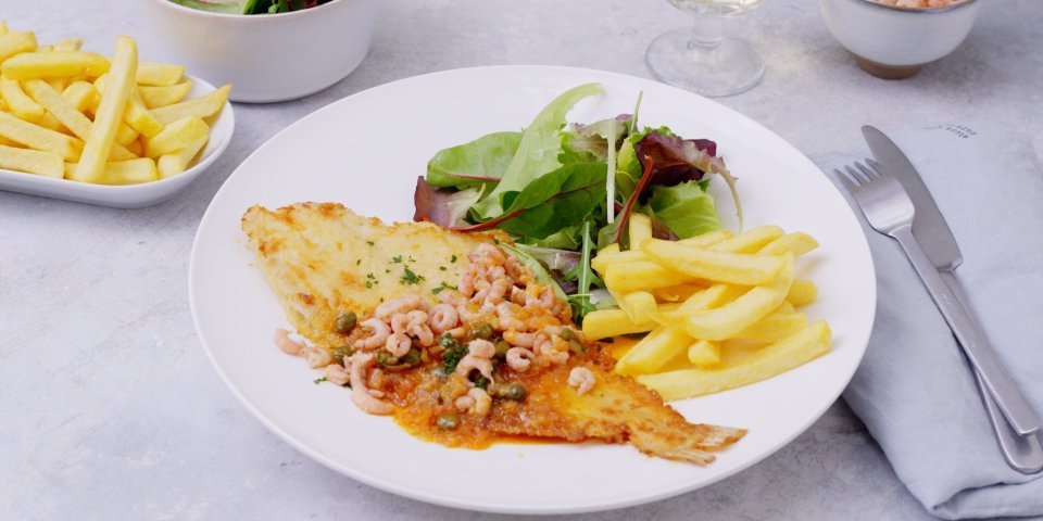Een bordje gevuld staat op tafel, klaar om te beginnen. Er ligt een gebakken schartong op met een citroensausje afgewerkt met garnaaltjes. Bijgerechtjes zijn een groene salade en verse frietjes.