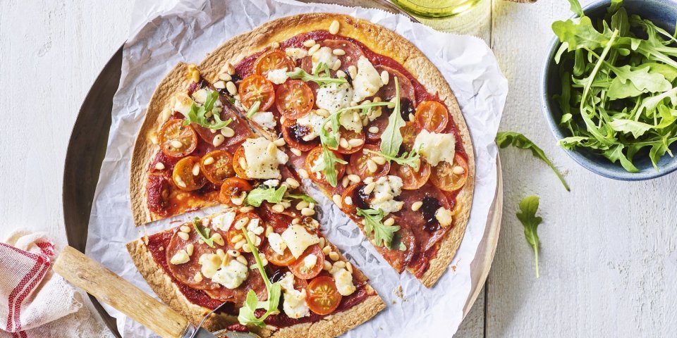 Snelle pizza-tortilla Een snelle pizza op tafelen toveren doe je met deze tortizza. De pizzabodem maakten we van een tortilla waar we lekkers aan toevoegde. Denk maar aan tomaatjes, salami en geitenkaas. We voegden ook nog een handje rucola toe voor de kleur. De pizza ligt al aangesneden op een groot bord.