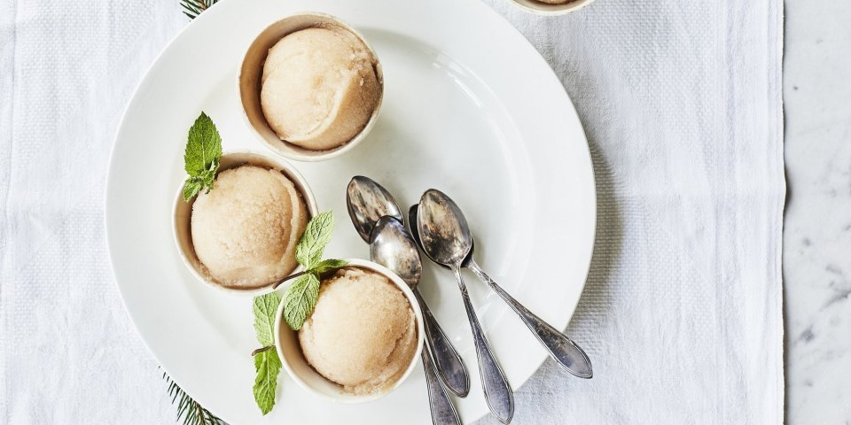 Sorbet van peer en citroen Drie sorbets staan op een wit rond bord, afgewerkt met een muntblaadje. De koffielepeltjes liggen ook op het witte bord, de tafel is aangekleed met takjes kerstboom.