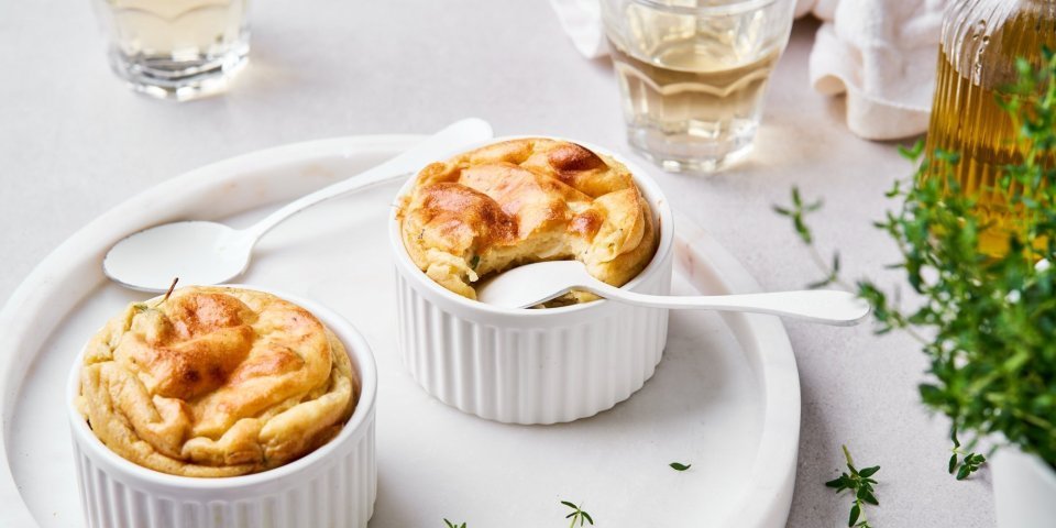 Soufflé van aardappelen en champignons Twee soufflees staan op een wit bord klaargemaakt. In eentje is al een hapje genomen en zit het lepeltje er nog in. Het gerecht is afgewerkt met verse tijm.