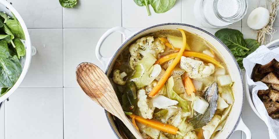 Stoofpotje van bloemkool, wortel en koolrabi Een lentestoofpotje boordevol groenten, denk maar aan bloemkool, wortel, koolrabi, prei en spinazie. De stoofpot staat op het aanrecht in een grote kookpot, rond de pot liggen nog enkele spinazieblaadjes en een flesje room.