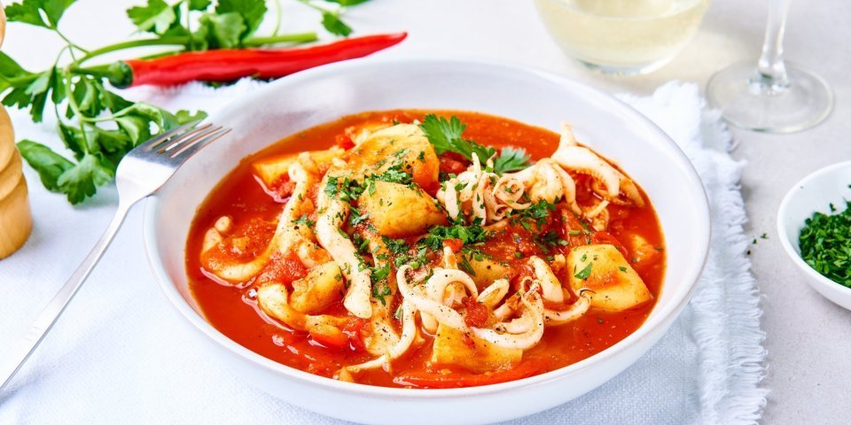 Stoofpotje van zeekat met aardappel en paprika in tomatensaus Een tomatenrood stoofpotje met vis staat op tafel. Het is een stoofpotje met stukjes paprika, aardappelen en tomatensaus.