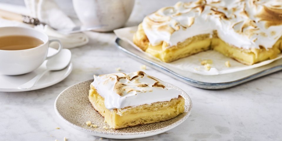 Taart van croissants, lemon curd en meringue Croissanttaart staat aangesneden op tafel, thee is opgediend en bordjes staan klaar. De meringue is mooi gekleurd door de brulébrander.