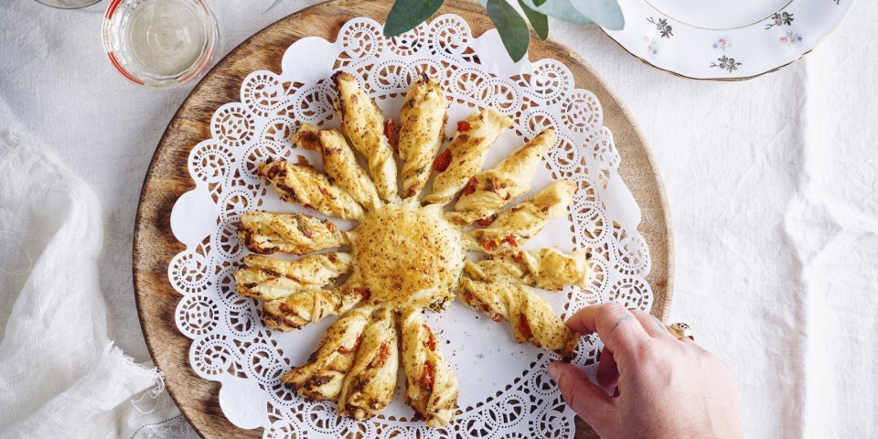 Tarte soleil met ricotta van berloumi en kerstomaat Een bladerdeeghapje met ricottakaas van bij ons en kerstomaatjes. Dit hapje is speciaal door de vorm, hij is nl gemaakt in de vorm van een zon. Hij ligt op een houten dienblad en er neemt een hand een zonnestraal om op te proeven.