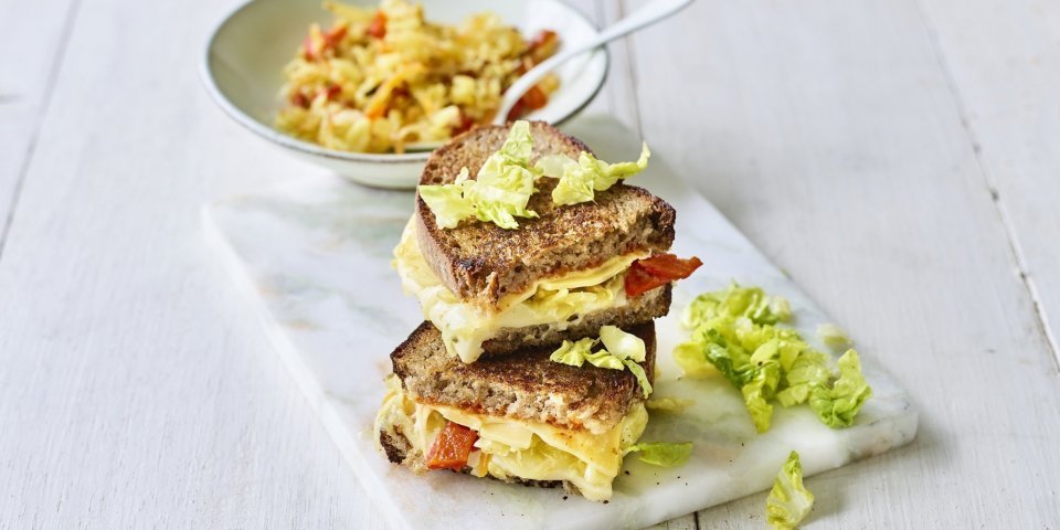 Een heerlijke cheesy toast ligt op een marmere snijplank. De toast is gevuld met 2 Belgische kazen, kimchi en chilisaus. 