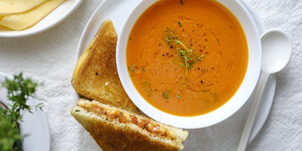 Tomatensoep van geroosterde tomaten met kaastoast Een heerlijke kom soep staat klaar op tafel in een wit kommetje. Wij serveren hem met een toast van kaas en tomaatjes. Een heerlijke en voedzame lunch.