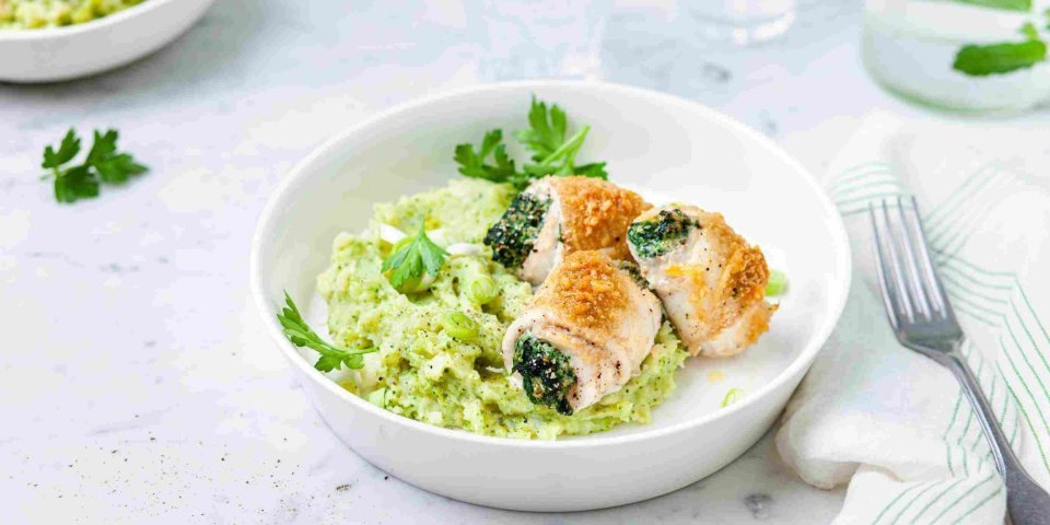 Tongrolletjes met broccolipuree Gevulde tongrolletjes met spinazie en ricotta liggen op een groene puree van broccoli en aardappel. Ze liggen in een diep bord waarbij een karaf- en waterglas langs staat.