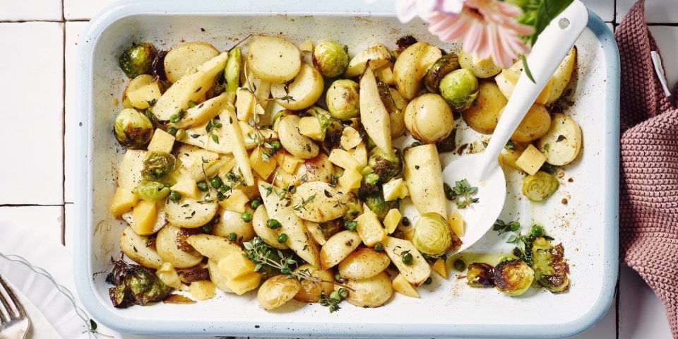 Een heerlijk geurende ovenschotel staat op het aanrecht. Het is een traybake van aardappelen met spruitjes, pastinaak en Beauvoordse brokkelkaas.