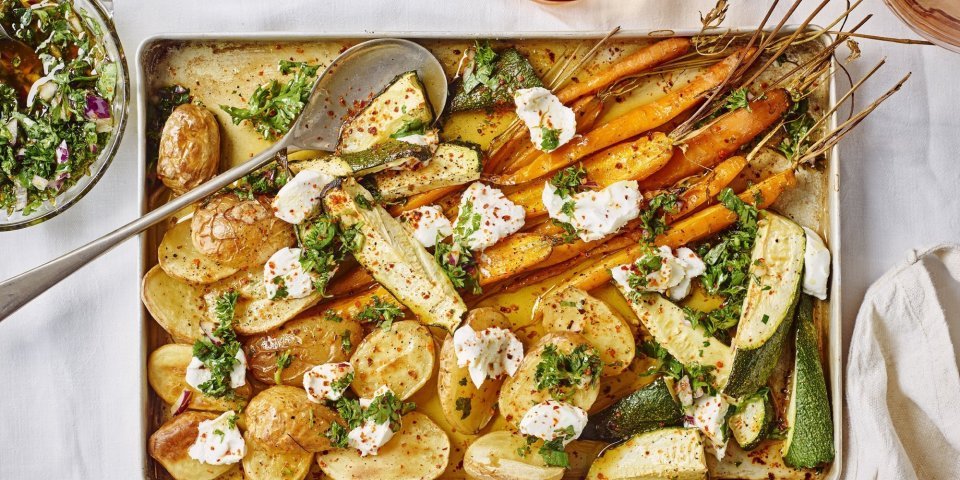 Traybake met krieltjes, wortel, courgette en geitenkaas Ovenplaat met gegrilde groentjes komt net uit de oven en staat al op tafel. Hij heeft warme kleuren van de gouden aardappelen naar de oranje wortelen. Hij is afgewerkt met toefjes geitenkaas en verse chimichurri.