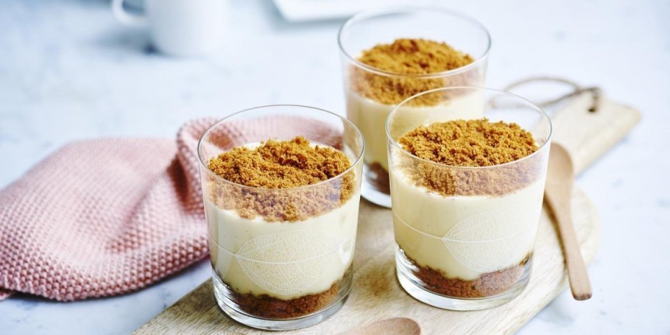 Op een houten plank staan 3 vanillepuddingen die afgewerkt zijn met speculaaskoekjes. Op de bodem liggen ook enkele koekjes om vol te genieten van de speculaassmaak.