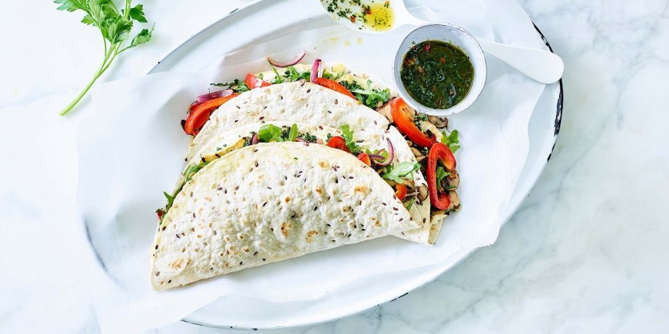Vegetarische quesadilla met geroosterde knolselder, champignons, paprika en Brugge Oud Vegetarische quesadilla gevuld met geroosterde knolselder, champignons, paprika en Brugge Oud. 2 stuks liggen gepresenteerd op een ovaal wit bord, samen met de vinaigrette in een potje apart. Takje verse koriander ligt er langs voor extra groen en sfeer aan het beeld mee te geven.