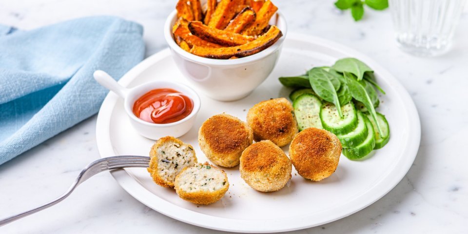 Visballetjes van wijting liggen op een wit bord met frietjes van pompoen erbij. Er staat ook een potje ketchup langs en een lichtblauwe servette. 