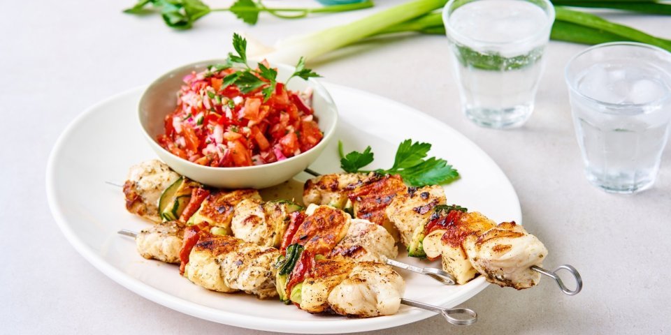 Visbrochette van zeeduivel en Berloumi met tomatensalsa Enkele gegrilde brochettes liggen op een serveerschaal samen met een potje tomatensalsa. De salsa zorgt voor een mooie rode kleur bij de zeeduivelspiesjes.