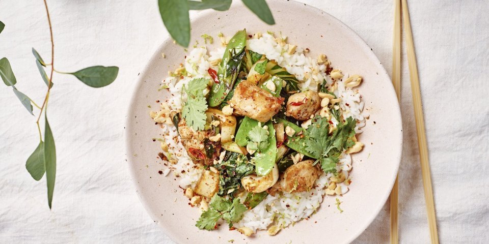 Een portie food is uitgeschept in een licht roze bord. Het is een portie rijst met daar bovenop de wok van konijn met paksoi en peultjes. Om af te werken zijn er wat pindanootjes toegevoegd en koriander.