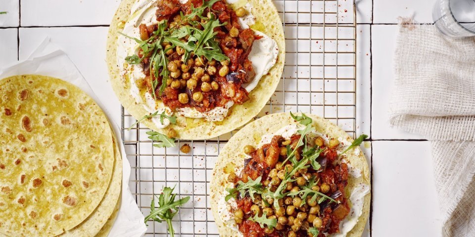 Wrap met roomkaas, geroosterde kikkererwten en een spread van aubergine en tomaten Twee wraps liggen op een ovenrooster klaargemaakt. Ze zijn belegd met roomkaas, tomatenspread en geroosterde kikkererwten. Er liggen nog enkele extra wraps langs. Het gerechtje is afgewerkt met enkele blaadjes rucola.