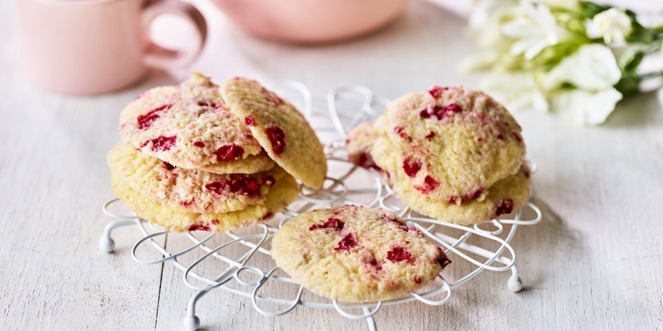 Zandkoekjes met frambozen Op een kleine taartrooster liggen enkele koekjes te drogen. De koekjes hebben rode vlekjes van de framboosjes. Er staat een theepot langs met al een uitgeschonken thee in bijpassende roze tas.
