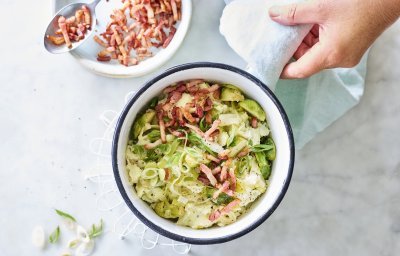 Smeuïge aardappelpuree met grofgehakte spruitjes en prei klaargemaakt in een kookpot. De kok in kwestie voegt de versneden lente-uitjes en gebakken spekjes toe als afwerking.