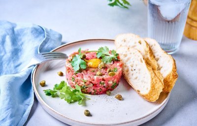 Een verse steak tartaar ligt in een mooi rondje op een bord. Bovenop ligt een kwarteleitje te blinken. 