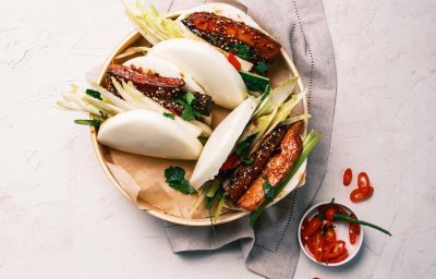 Op het aanrecht staat een groot rond bord met hierin 4 klaargemaakte bao buns. Er staat een klein potje langs met fijngesneden chili voor extra pit toe te voegen.