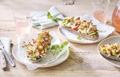 Er staan 3 bordjes klaar op een houten tafel. De ideale lunch om te benuttigen buiten in de zon. De halve broodjes zijn belegd met kruidige kip en verse groentjes. 