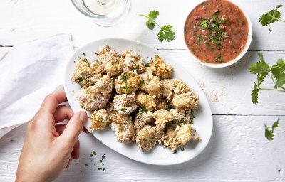 Krokante bloemkoolroosjes als aperitiefhapje, liggen klaar op een ovaal wit bordje. Er staat een pittige tomatensaus langs om te dippen. Tijd voor de apero te starten. 