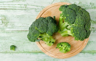 Twee groene broccoli's liggen op houten snijplank, klaar om roosjes uit te snijden en klaar te maken.