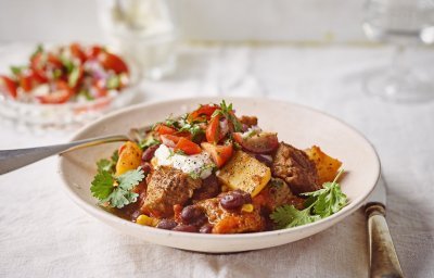 Stoofvlees gemaakt met de smaken van een chili con carne, heerlijk! Er is een portie uitgeschept in een diep bord en staat op een gedekte tafel. In de achtergrond staat de tomatensalsa en zure room om het gerechtje helemaal af te werken.