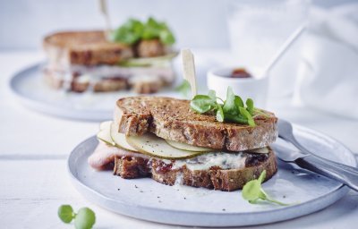 Een heerlijk croque van bruin brood met ham, schijfjes peer en blauwes chimmelkaas. Dit op een licht blauw bord met bestek en vijgenconfituur bij.