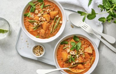 Twee heerlijke curry staan uitgeschept op tafel. Ze hebben een mooie oranje kleur door, jawel, de curry pasta. Ze staan beiden op een poseleinen dienplateau met bestek en een potje pina- en hazelnoten. 