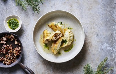 Dumplings liggen op een beige bordje, er werd een dumpling opengesneden. Zo krijg je een kijkje in de vulling op basis van boschampignons en gerookt spek. 