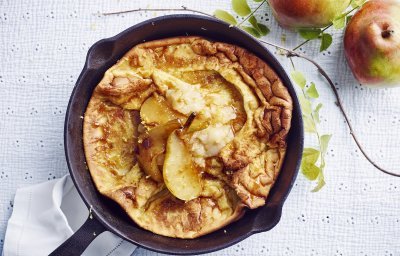 Een ovenpannenkoek met heerlijke peertjes, hij komt net uit de oven en ligt nog in de pan. Er liggen 2 verse peperen langs.