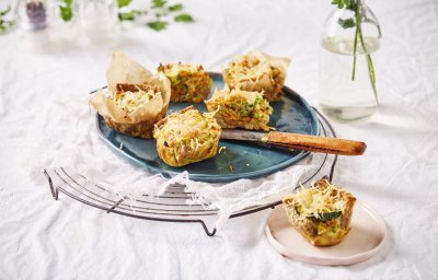 Op tafel staat een taartrooster met hierop enkele eimuffins. Ze zijn gemaakt van een sneetje brood als bodem en gevuld met groenten en eieren. Eentje werd aangesneden op een klein bordje. 