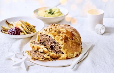 Rond gehaktbrood omhuld met bladerdeeg waarop sterren in bladerdeeg zijn teogevoegd. In het beeld liggen ook het gebraiseerd witloof met veenbessencompote en de puree. Kerstlampjes zien je flou in de foto.